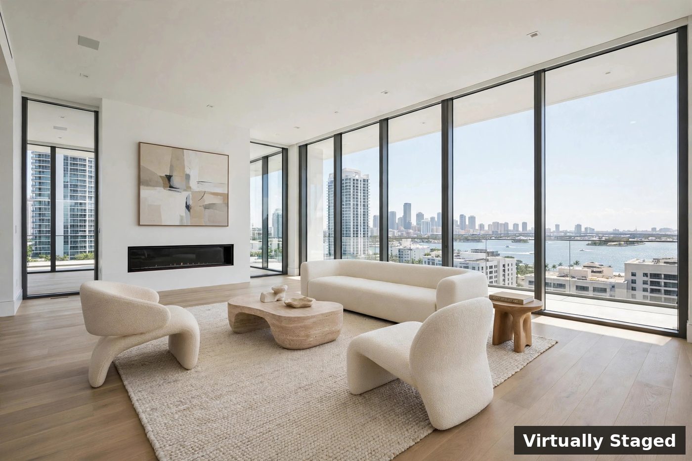 The same high-rise living room virtually staged with a modern ivory sofa, sculptural chairs, a stone coffee table, a rug, and abstract art above the fireplace; the words Virtually Staged appear as a label in the corner of the image
