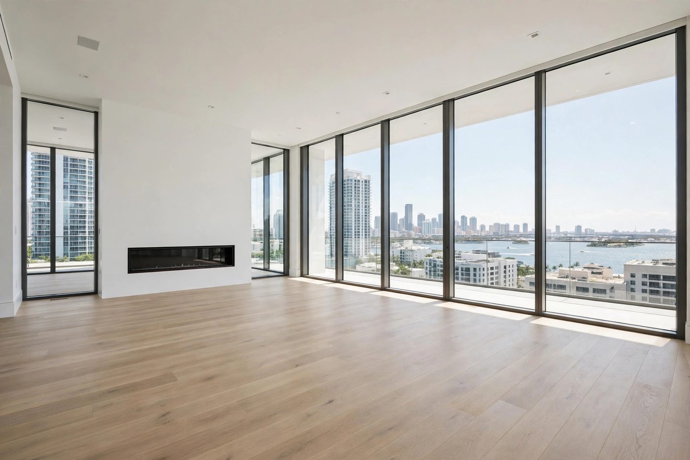 Original photograph of an empty luxury high-rise living room with floor-to-ceiling windows, a city and water view, and a linear fireplace — unstaged and untouched